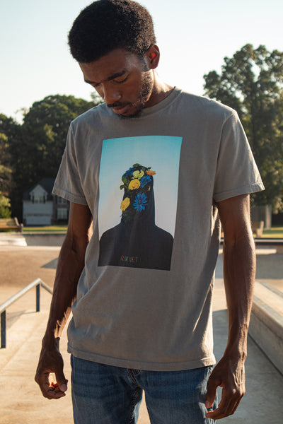 Young black male model wearing a grey graphic tee at a skatepark. Skateboard wear and streetwear style.